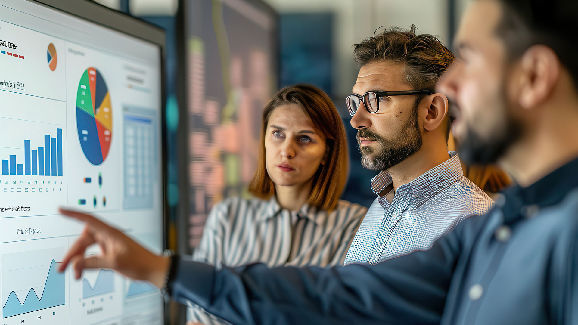 Co-workers analyzing charts on a large monitor