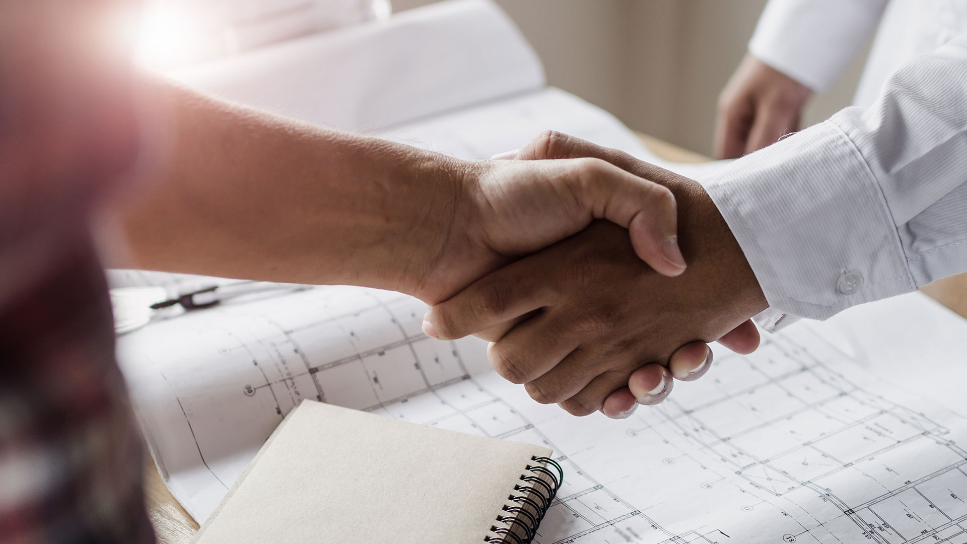 Colleagues handshaking over building plans.