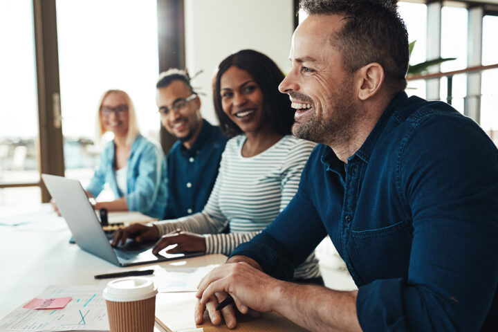 Mature businessman laughing while sitting with a diverse group of coworkers during a meeting in an office