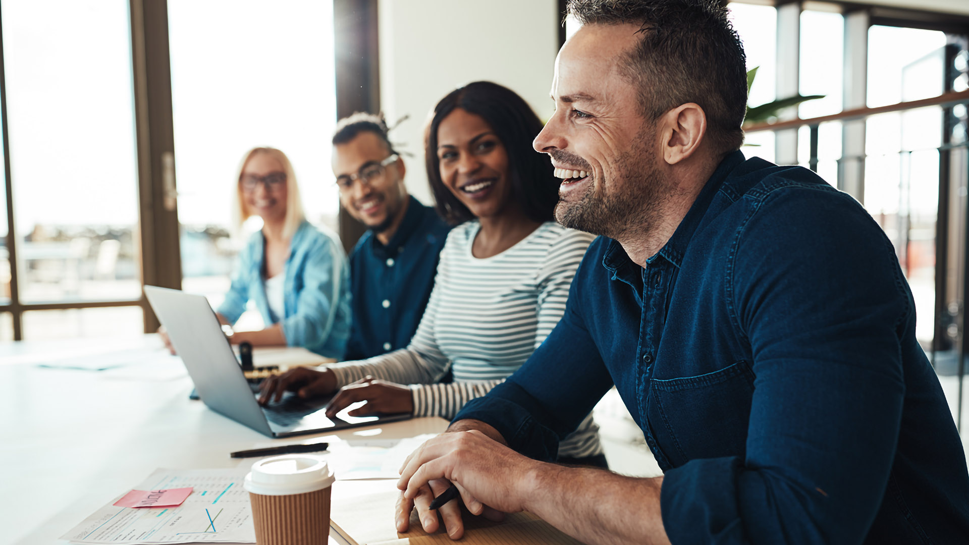 Mature businessman laughing while sitting with a diverse group of coworkers during a meeting in an office