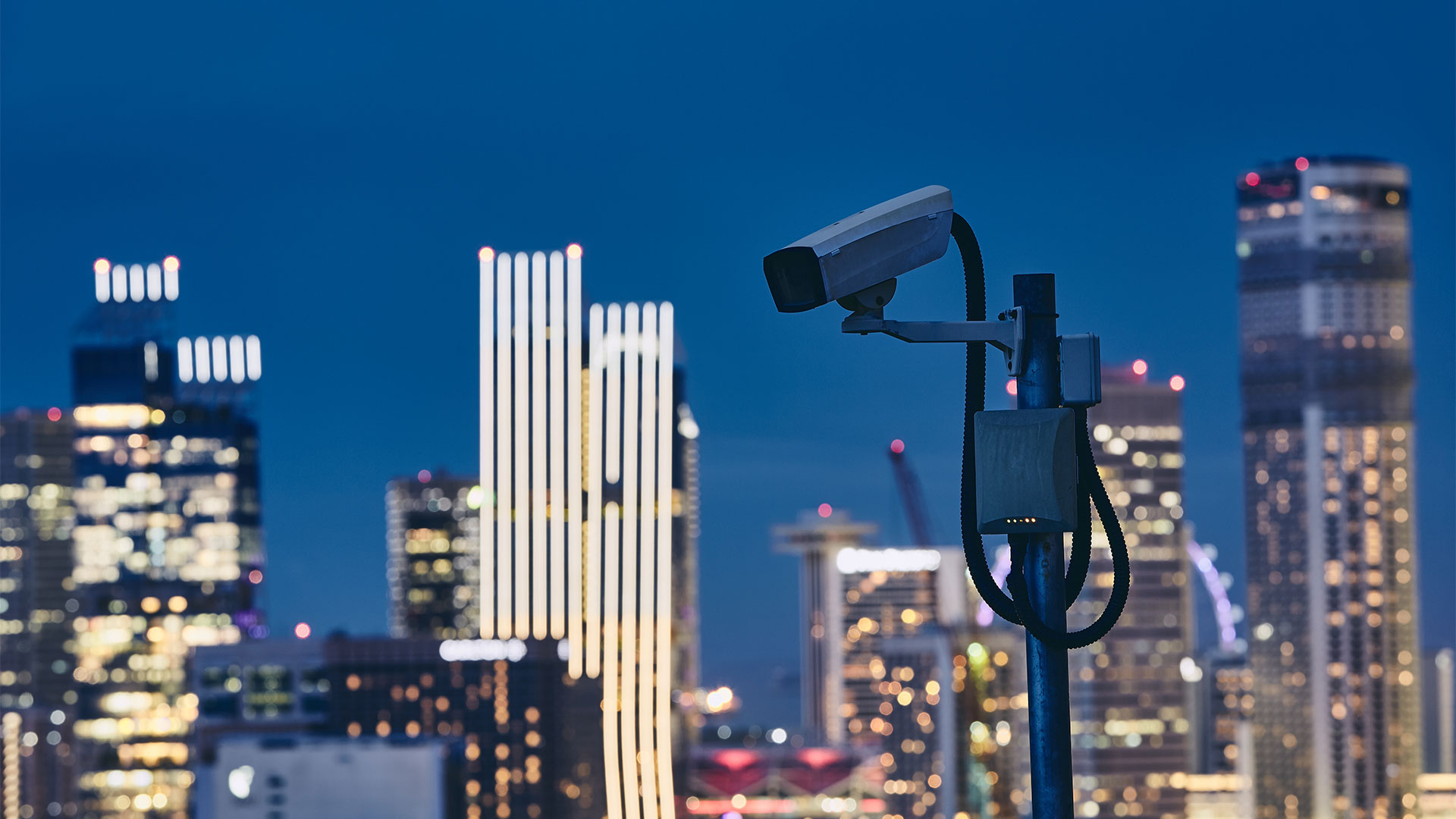 Security camera against illuminated urban skyline at night. Concept of surveillance and safety.